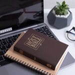 An open Bible surrounded by business items on a desk, signifying the importance of bible verses in the growth and success of Christian entrepreneurship for Business Scriptures.